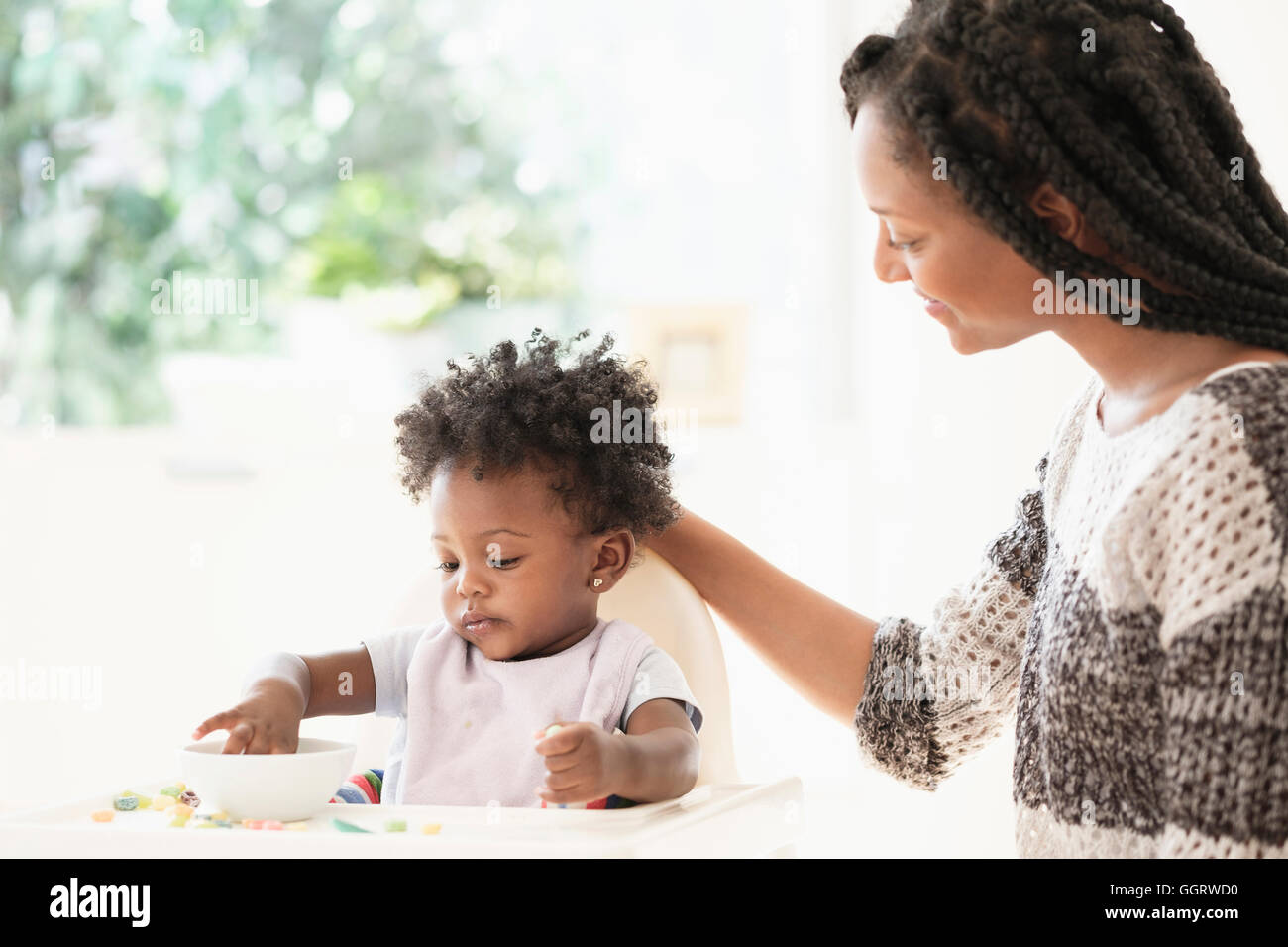 Femme noire en regardant sa petite fille de manger les céréales dans une chaise haute Banque D'Images