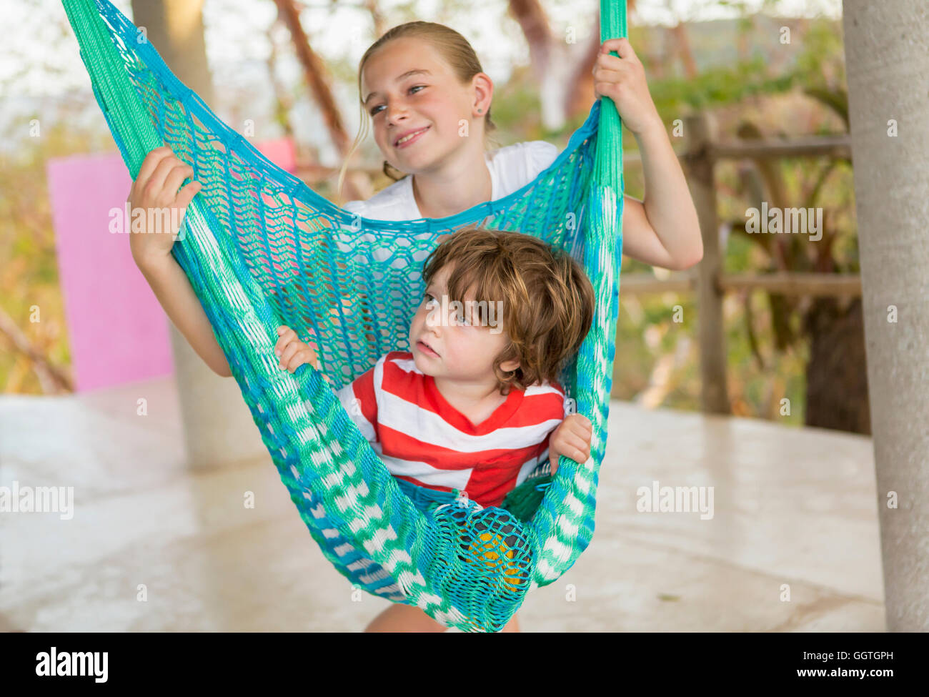 Young boy sitting in hammock tenu par soeur Banque D'Images