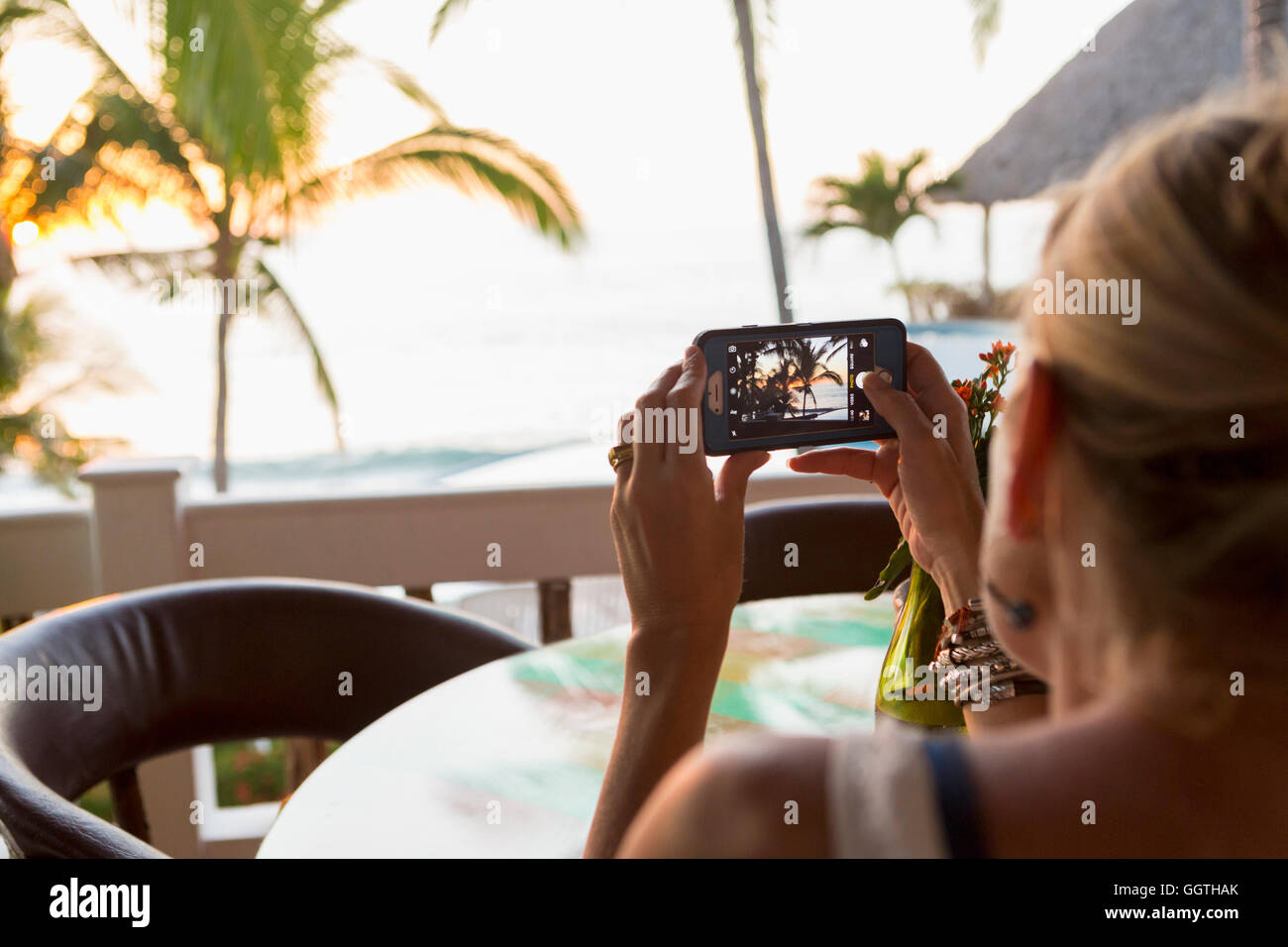 Caucasian woman photographing sunset at beach Banque D'Images