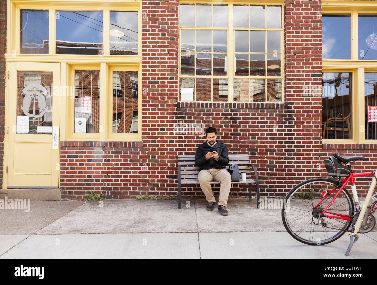 Hispanic man sitting on bench ville using cell phone Banque D'Images