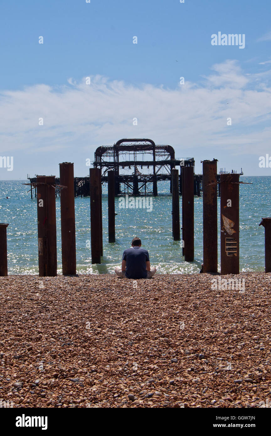 Homme assis sur la plage en face de la jetée de l'Ouest, Brighton, England, UK Banque D'Images
