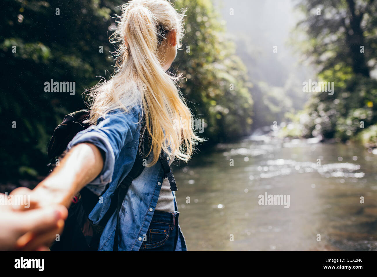 Jeune femme menant son petit ami sur la forêt randonnée. Point de vue tourné de couple crossing le ruisseau se tenant la main. Banque D'Images