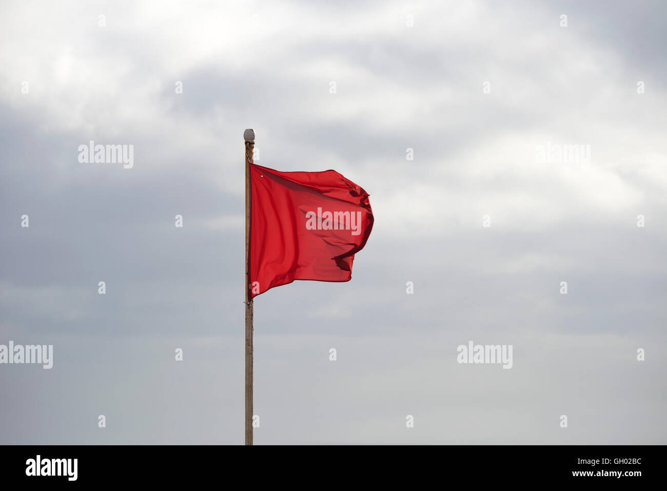 Drapeau rouge sur une plage en agitant au-dessus de ciel nuageux Banque D'Images