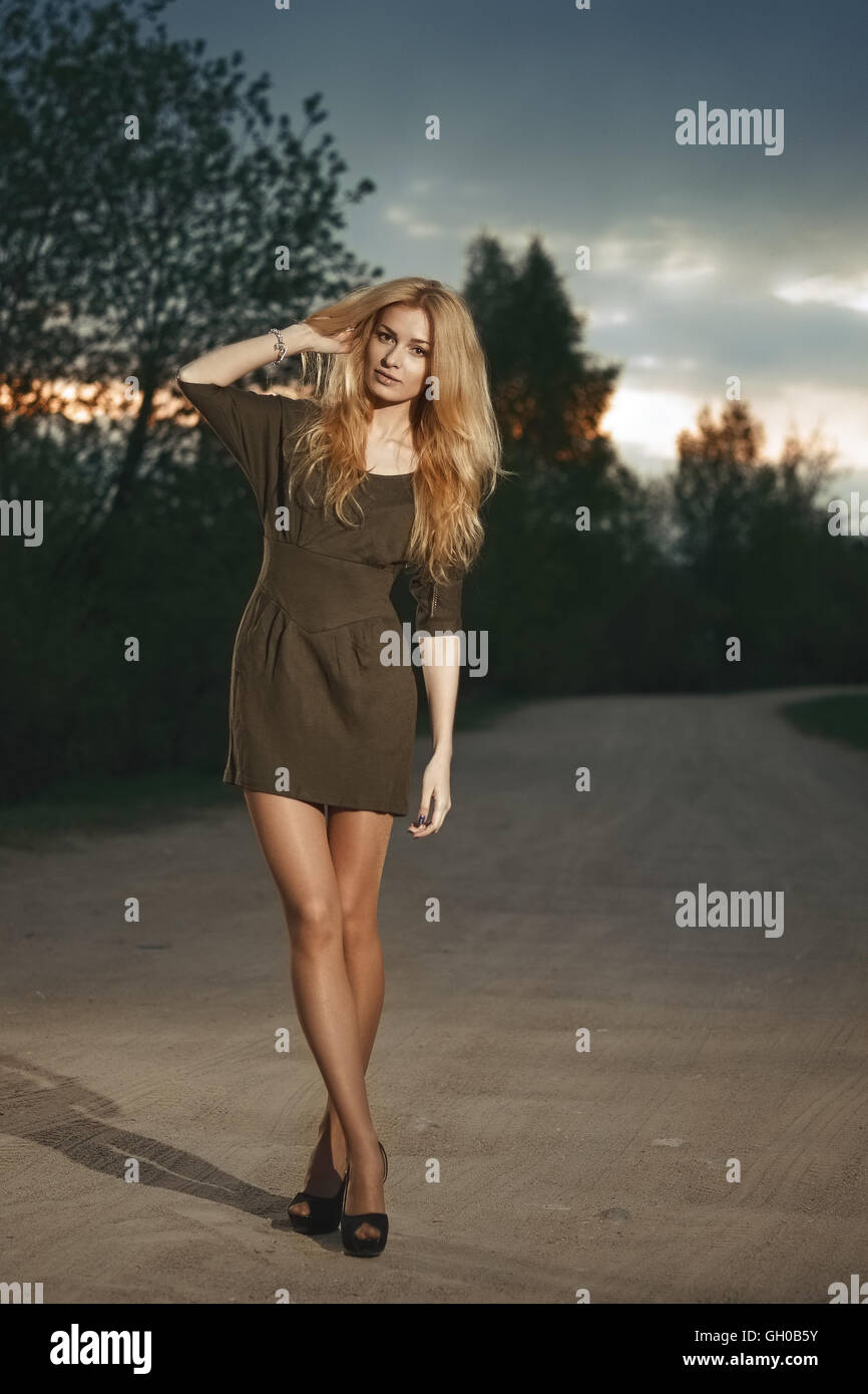 Portrait d'une jolie femme blonde à l'heure du coucher du soleil sur la route. De longues jambes et des talons hauts. Banque D'Images