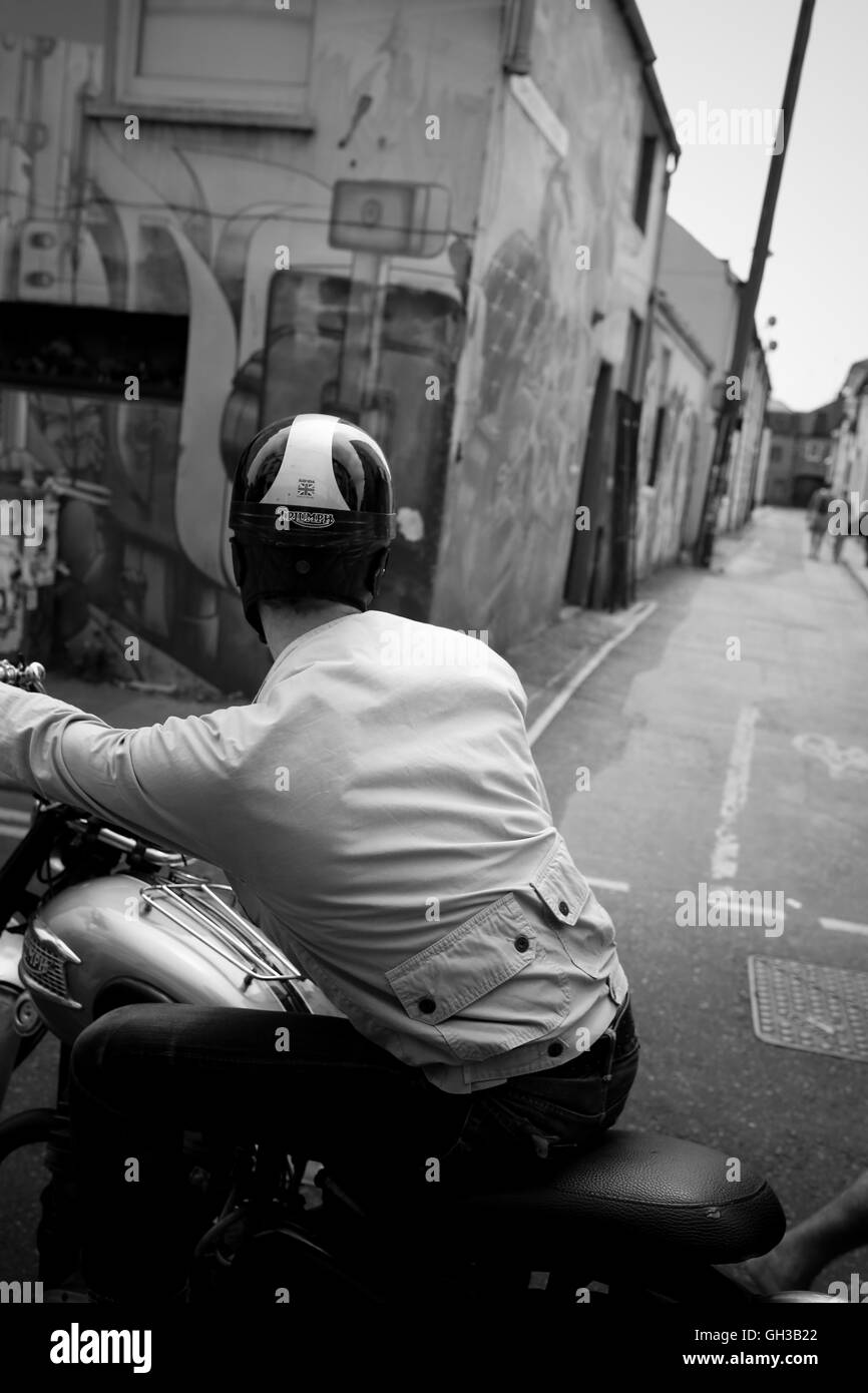 Un homme sur une moto à l'arrêt et regardant en bas d'une petite rue où il peut voir un couple de gens waling au loin. Banque D'Images