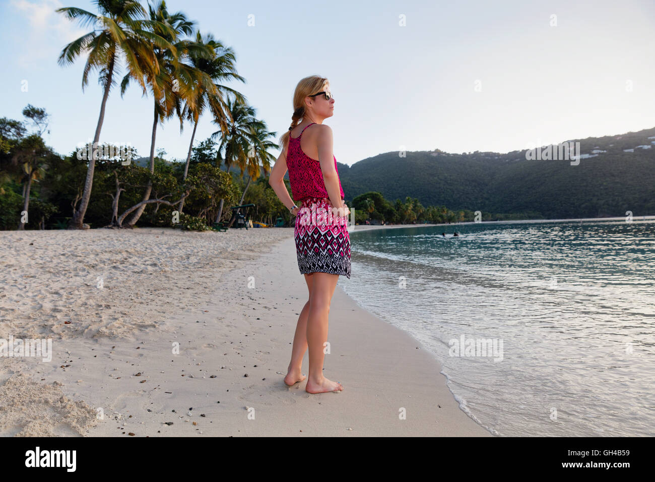 Low Angle View of a Woman Standing sur une plage des Caraïbes pieds nus dans une robe d'été au coucher du soleil, heure Magens Bay, St Thomas, Vir Banque D'Images