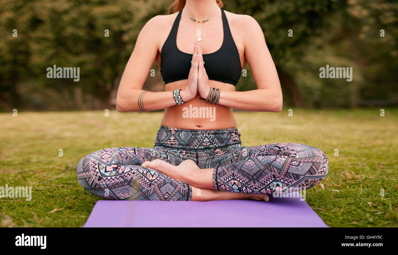 Remise en forme de tir horizontal woman sitting on exercise mat avec ses mains jointes. Les femmes pratiquant le yoga en plein air dans le parc. Banque D'Images