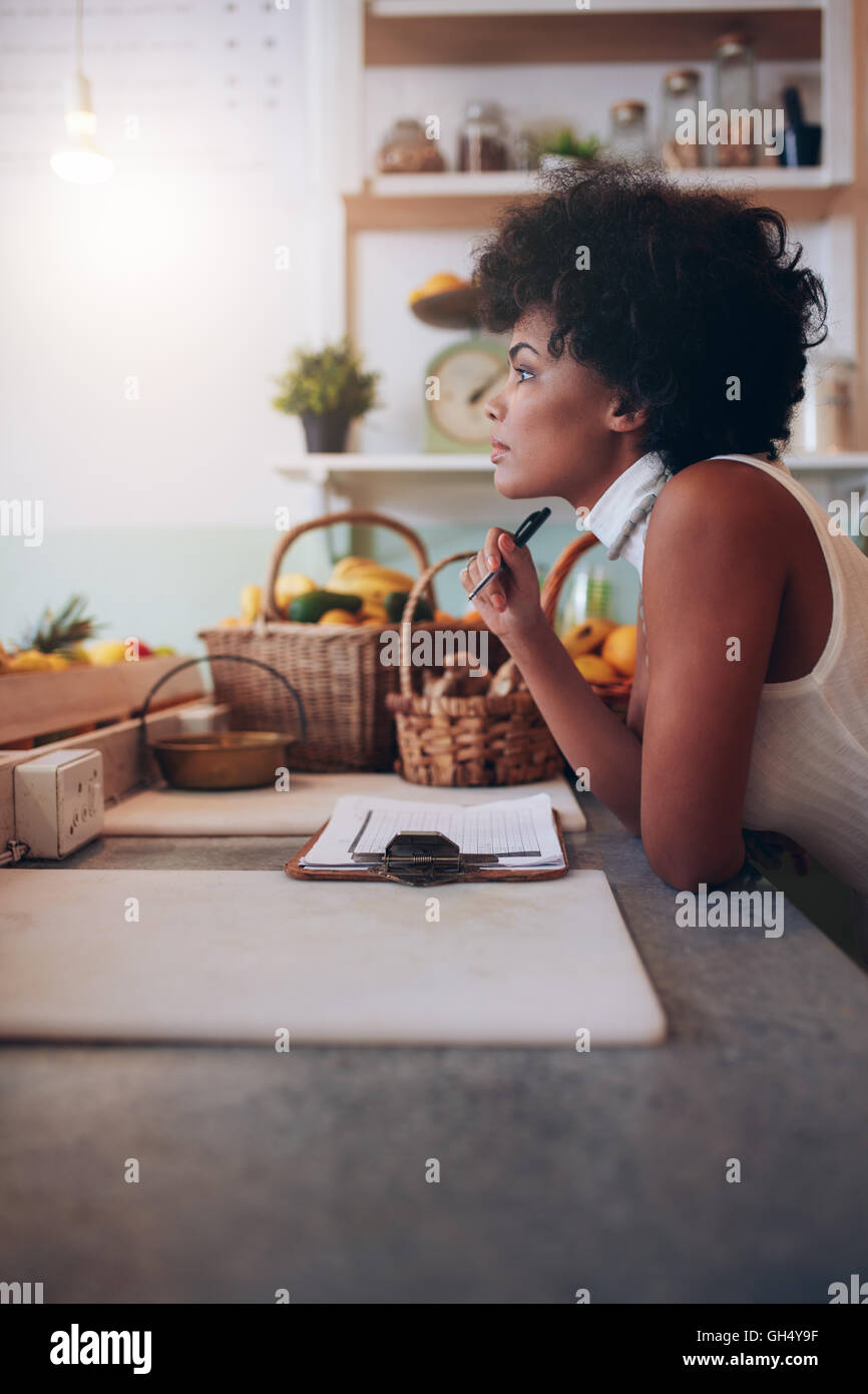 Side portrait of young woman standing au comptoir de bar de jus à l'écart et la pensée. Femme africaine sérieuse bar à jus propriétaire. Banque D'Images