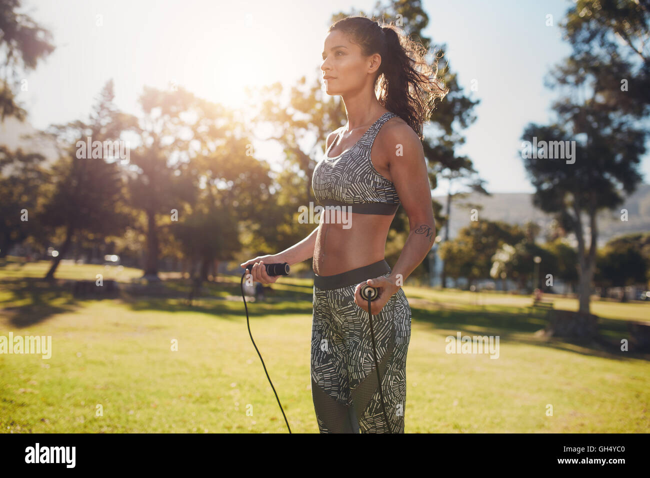 Plan extérieur d'une femme déterminée sautant dehors dans la nature. femme de fitness exerçant avec corde à sauter dans un parc par une journée ensoleillée. Banque D'Images