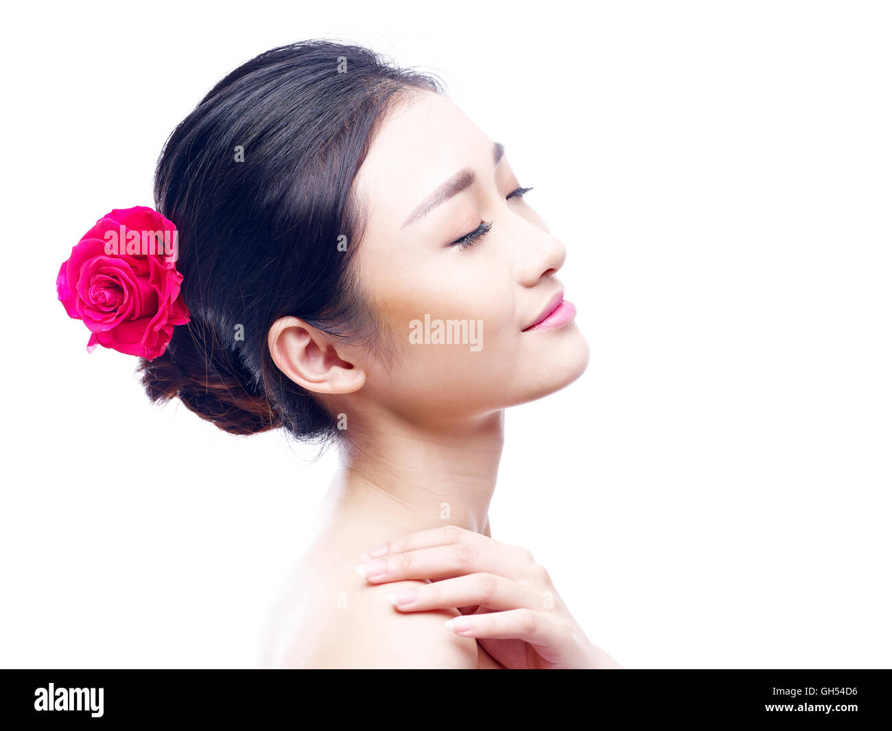 Portrait d'une jeune et belle femme asiatique, les yeux clos, vue latérale, rose rouge dans les cheveux, isolé sur fond blanc. Banque D'Images