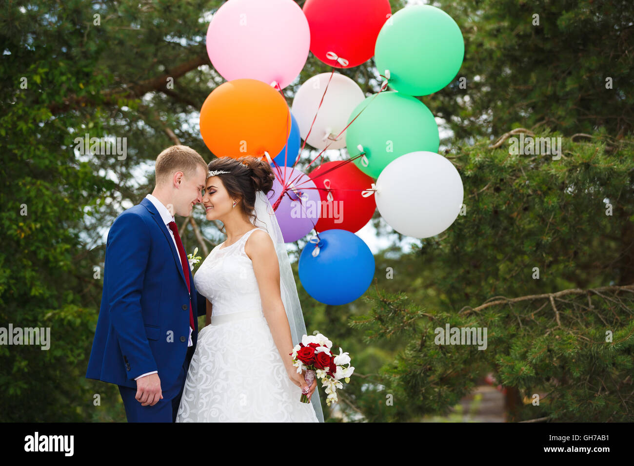 Jeune couple de mariage avec des ballons colorés serrant dans la forêt de pins Banque D'Images