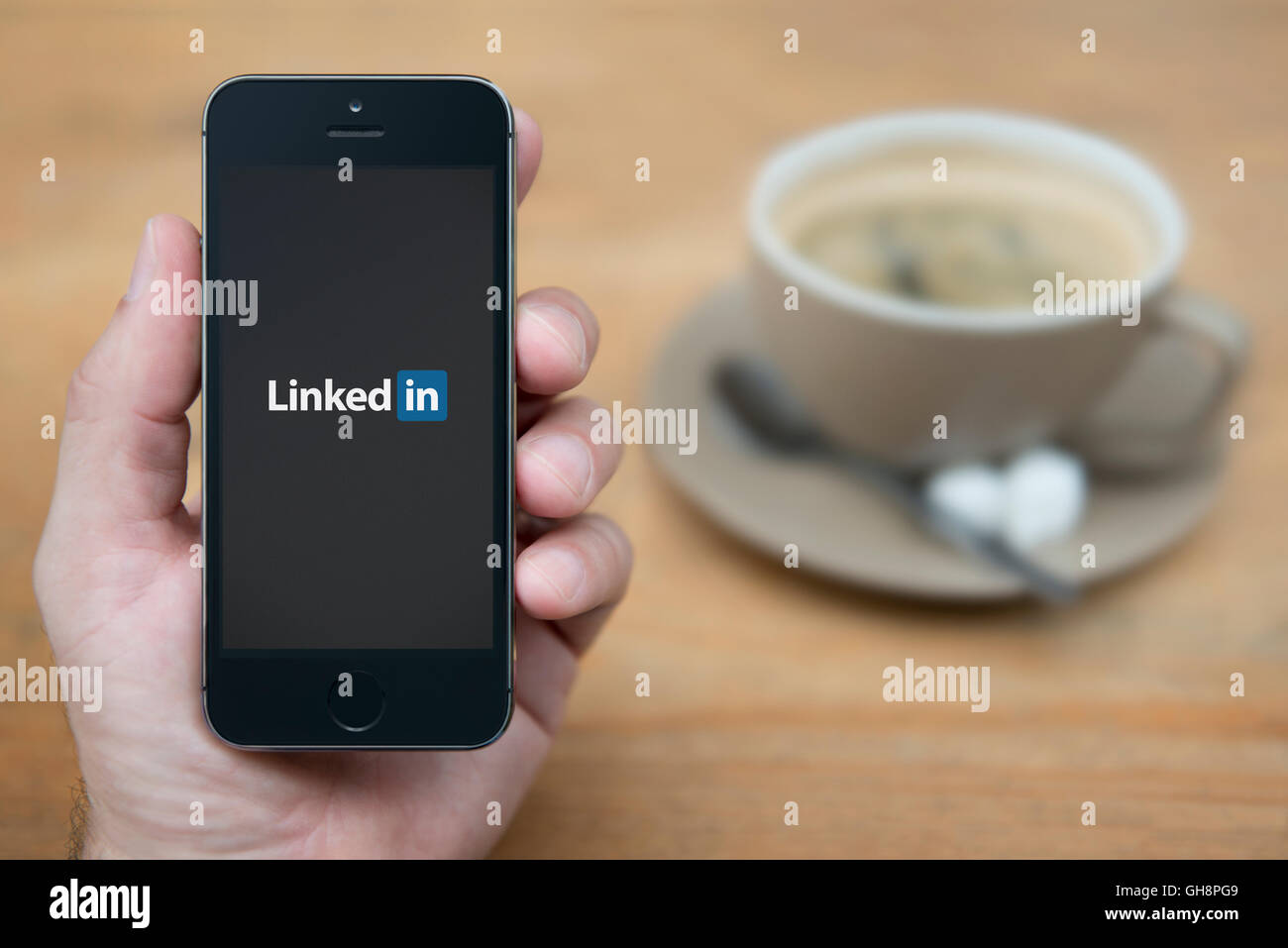Un homme se penche sur son iPhone qui affiche le logo de Linkedin, tandis qu'assis avec une tasse de café (usage éditorial uniquement). Banque D'Images