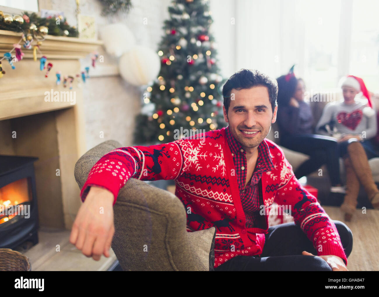 Portrait smiling man in Christmas sweater assis dans la salle de séjour Banque D'Images