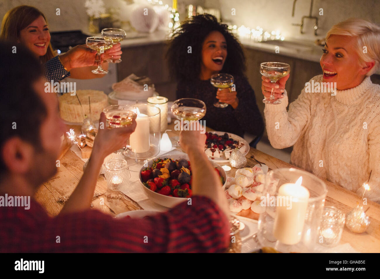 Amis enthousiastes toasting champagne verres aux chandelles dîner de Noël Banque D'Images