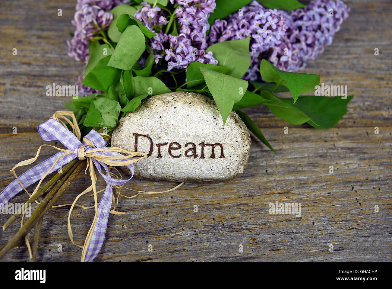 Bouquet de lilas avec le mot rêve sculpté dans une pierre sur bois rustique. Banque D'Images