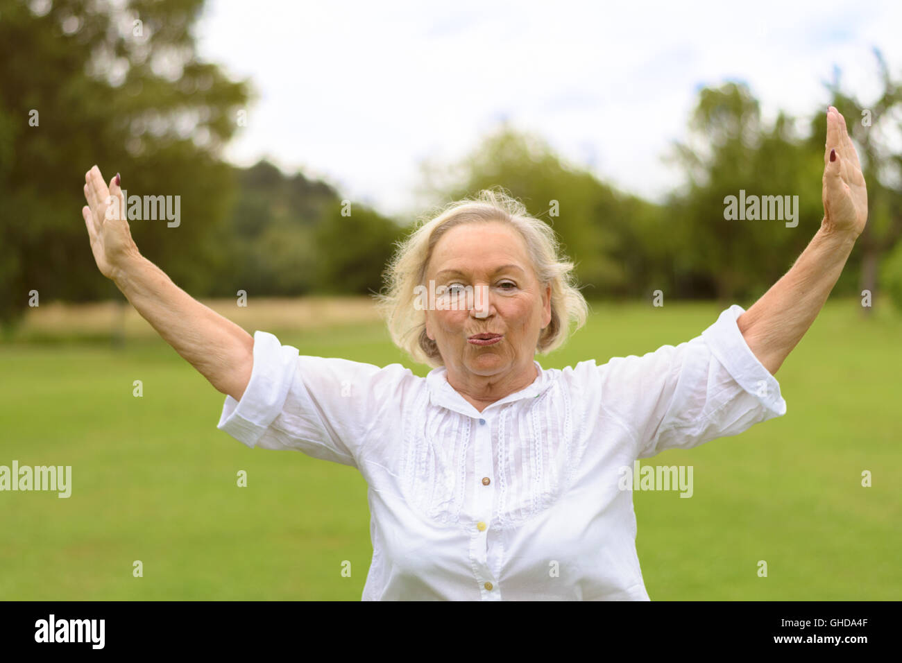 Seule belle senior woman in white rolled up long sleeve blouse de l'exercice à l'extérieur sur l'herbe verte with copy space Banque D'Images