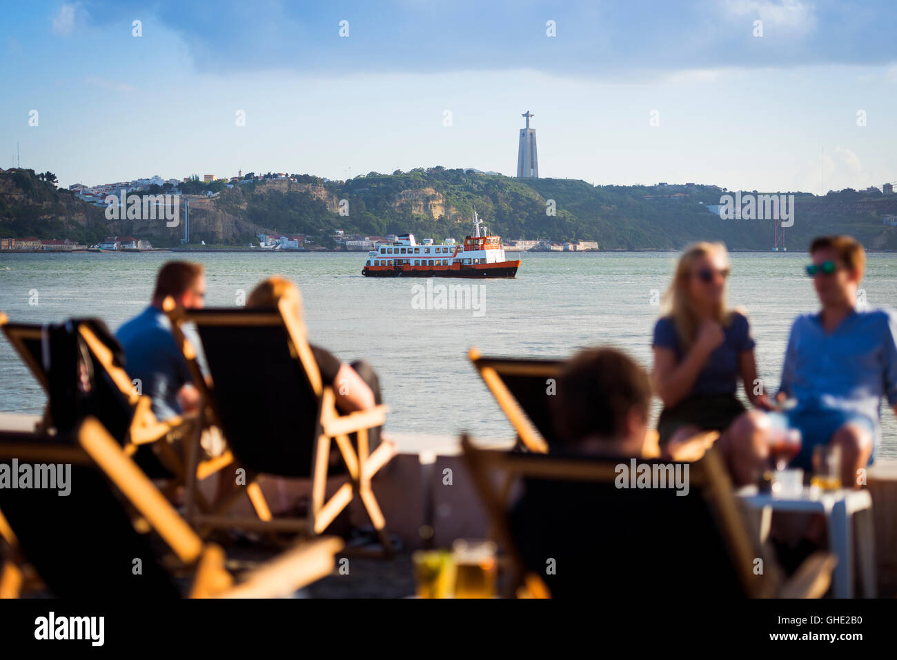 Les gens dans une esplanade à Lisbonne, Portugal, par le Tage, avec un bateau à passagers (cacilheiro) traversant le Tage ; Conc Banque D'Images