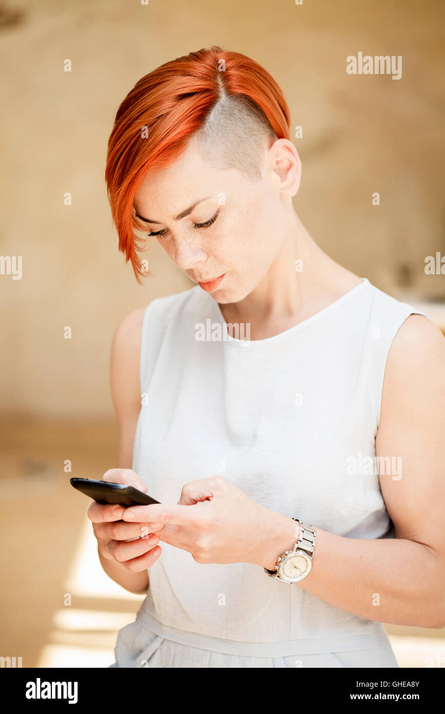 Femme cheveux rouge avec le côté coiffure rasée en utilisant un téléphone mobile Banque D'Images