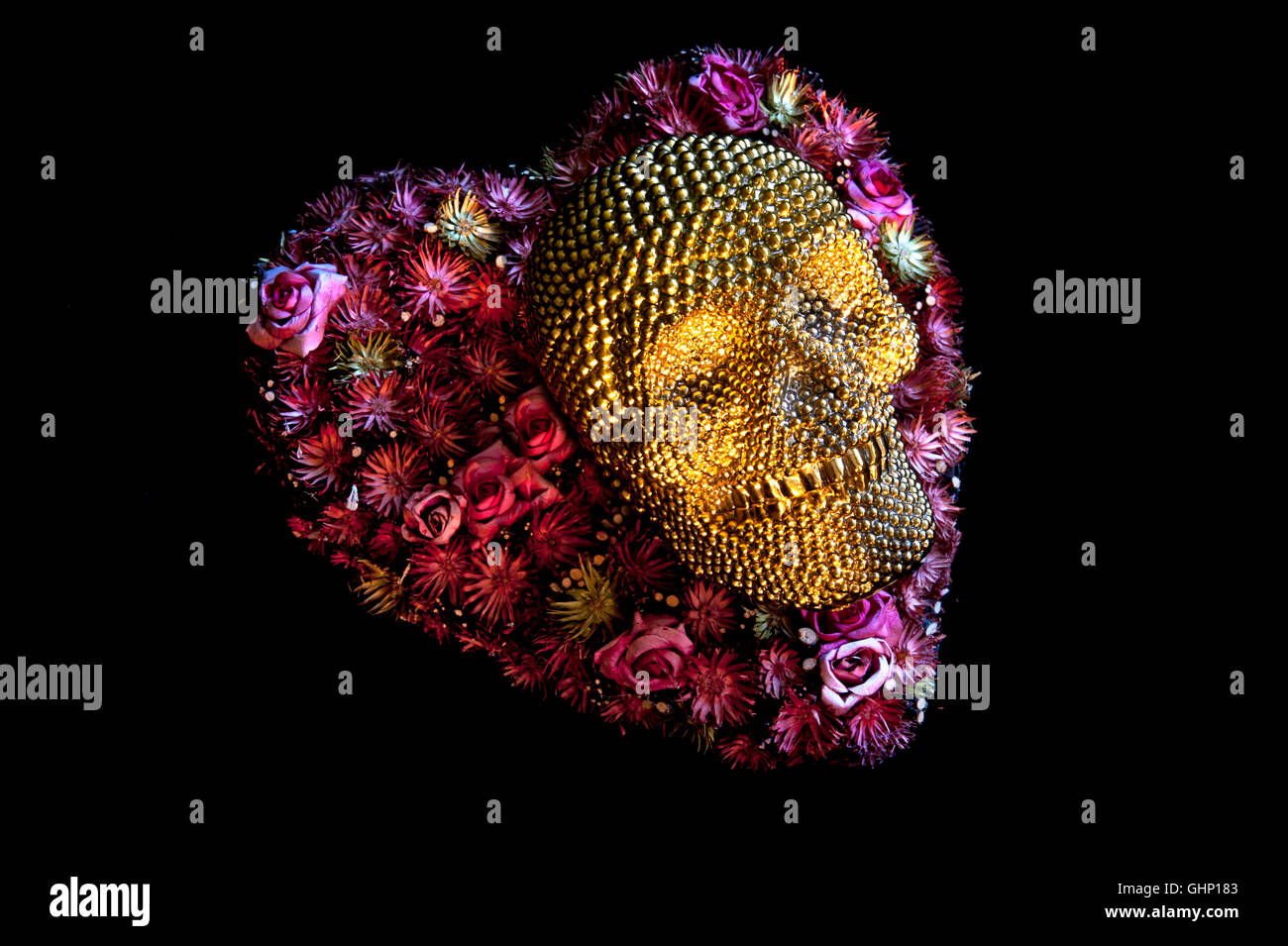 Concept image of gold crâne allongé en forme de cœur sur l'arrangement de fleurs sur fond noir Banque D'Images