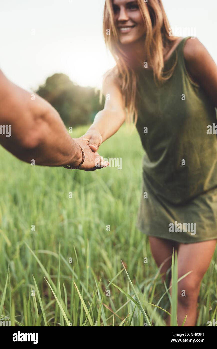 Shot of woman holding part de son petit ami et se tenant dans le champ d'herbe. Jeune couple aimant on meadow en plein air. Banque D'Images