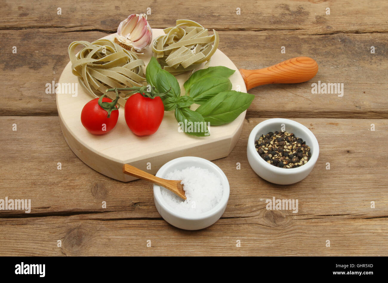 Tagliatelles à l'ail, les tomates, le basilic, le sel et le poivre sur une planche en bois sur une table en bois patiné Banque D'Images