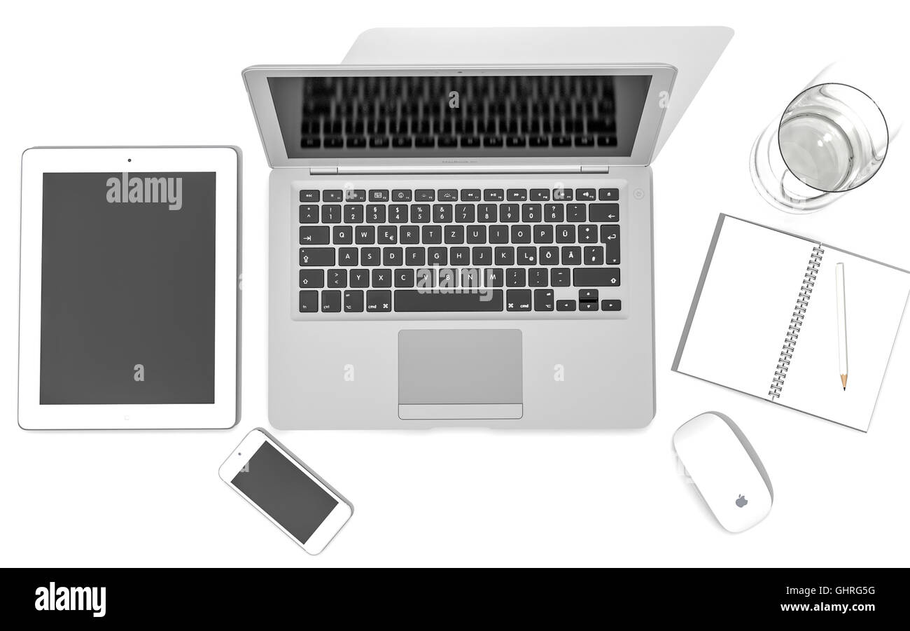 IPad, iPhone 5, Macbook Air et magic mouse d'Apple sur un bureau avec un verre d'eau et un carnet de notes et crayon Banque D'Images