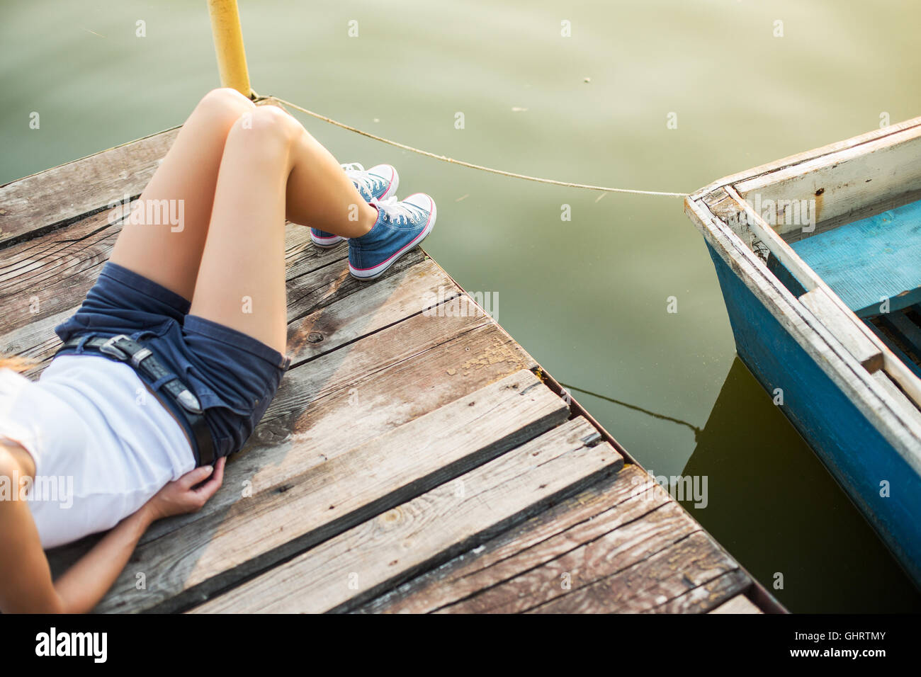 De vie de plein air view of young woman wearing jeans sneakers assis sur une jetée en bois à l'eau Banque D'Images