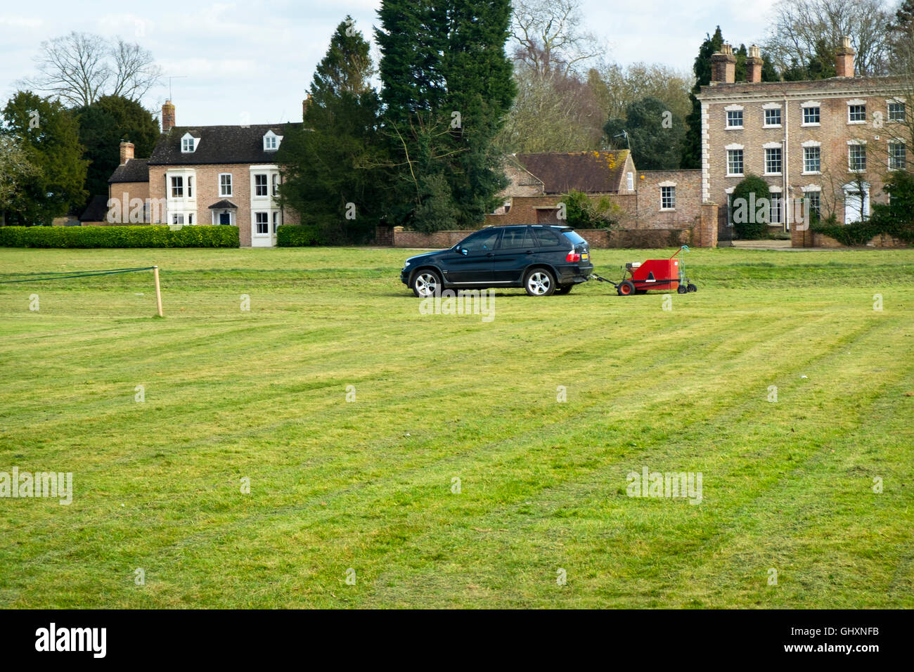 Remorquage d'une machine de coupe avec une voiture BMW. Tondre le terrain de cricket à Frampton sur Severn, Gloucestershire, Royaume-Uni Banque D'Images