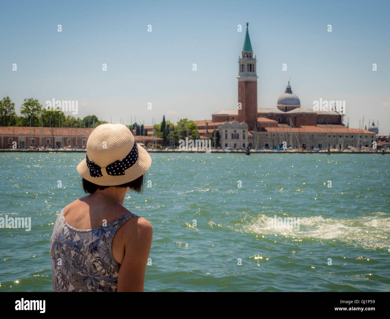 Vue arrière d'une femme, portant un chapeau de paille, assise sur un banc à l'ensemble de l'église et de l'île de San Giorgio Maggi Banque D'Images