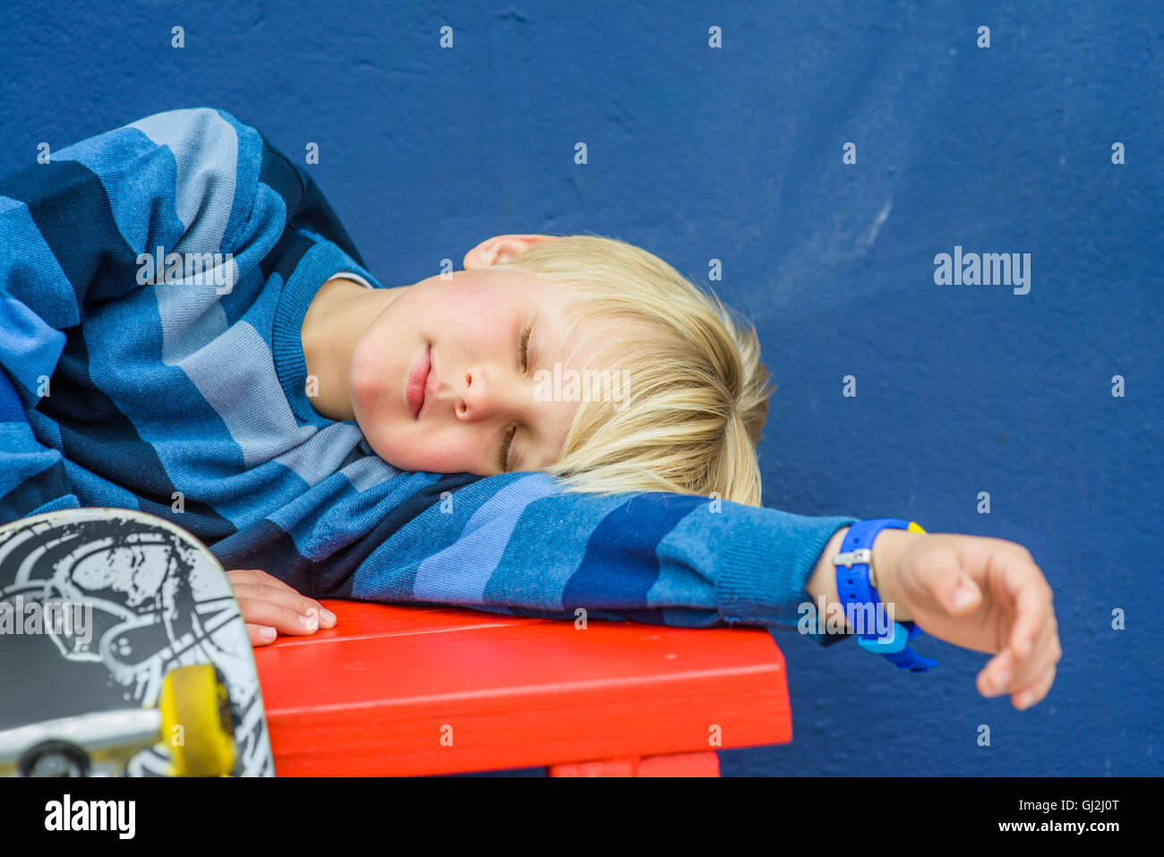 Garçon avec skateboard endormi sur le banc rouge Banque D'Images