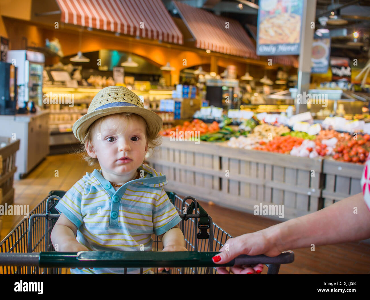 Baby Boy wearing straw hat sitting in shopping trolley Banque D'Images