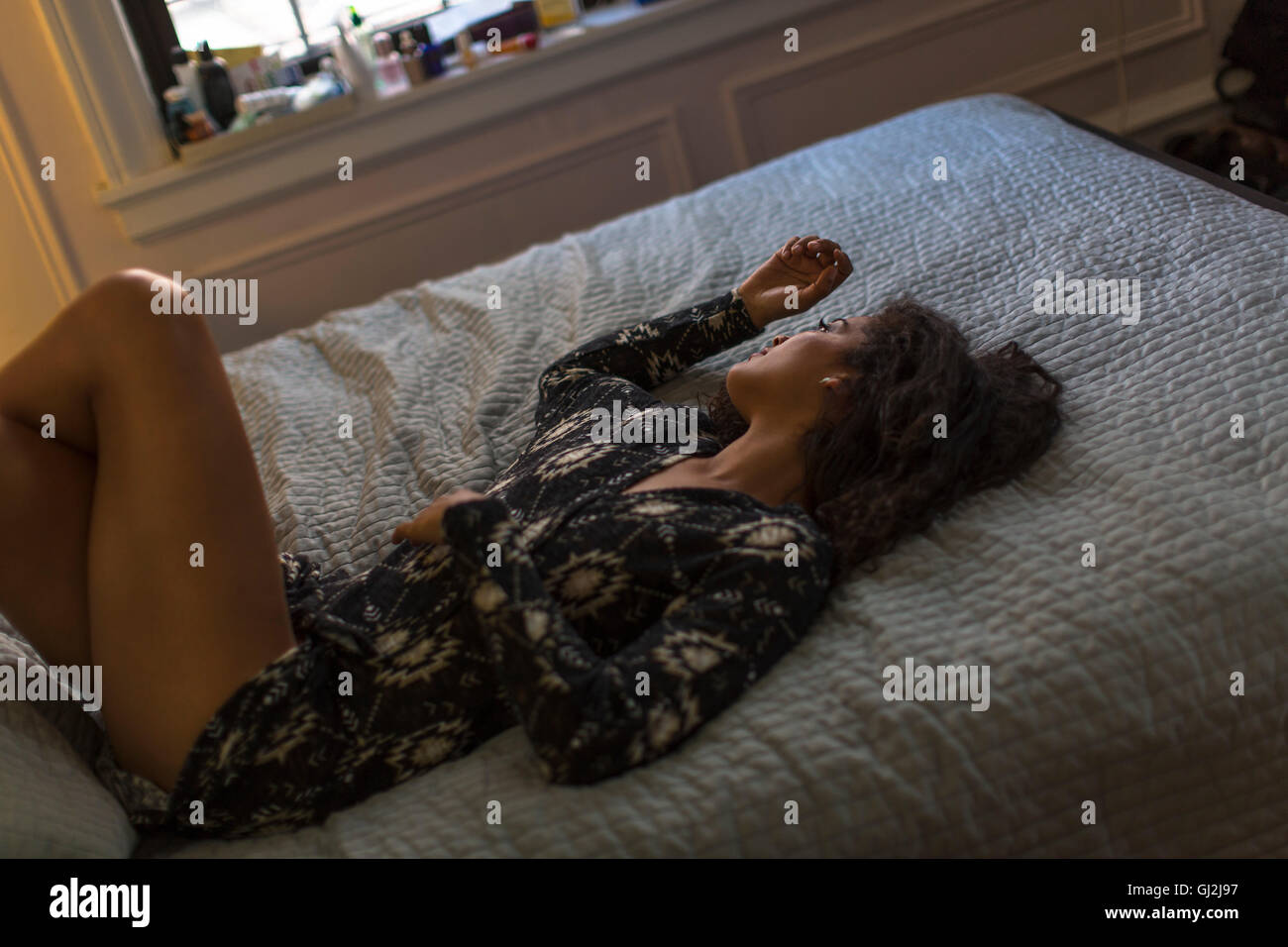 Young woman relaxing on bed, à la fenêtre de Banque D'Images