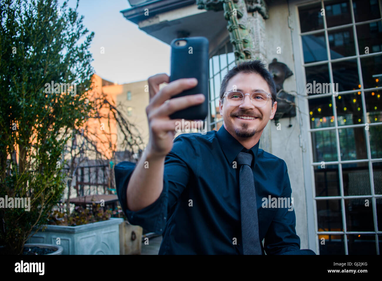 Jeune homme assis à l'extérieur, holding smartphone, sur appel vidéo Banque D'Images