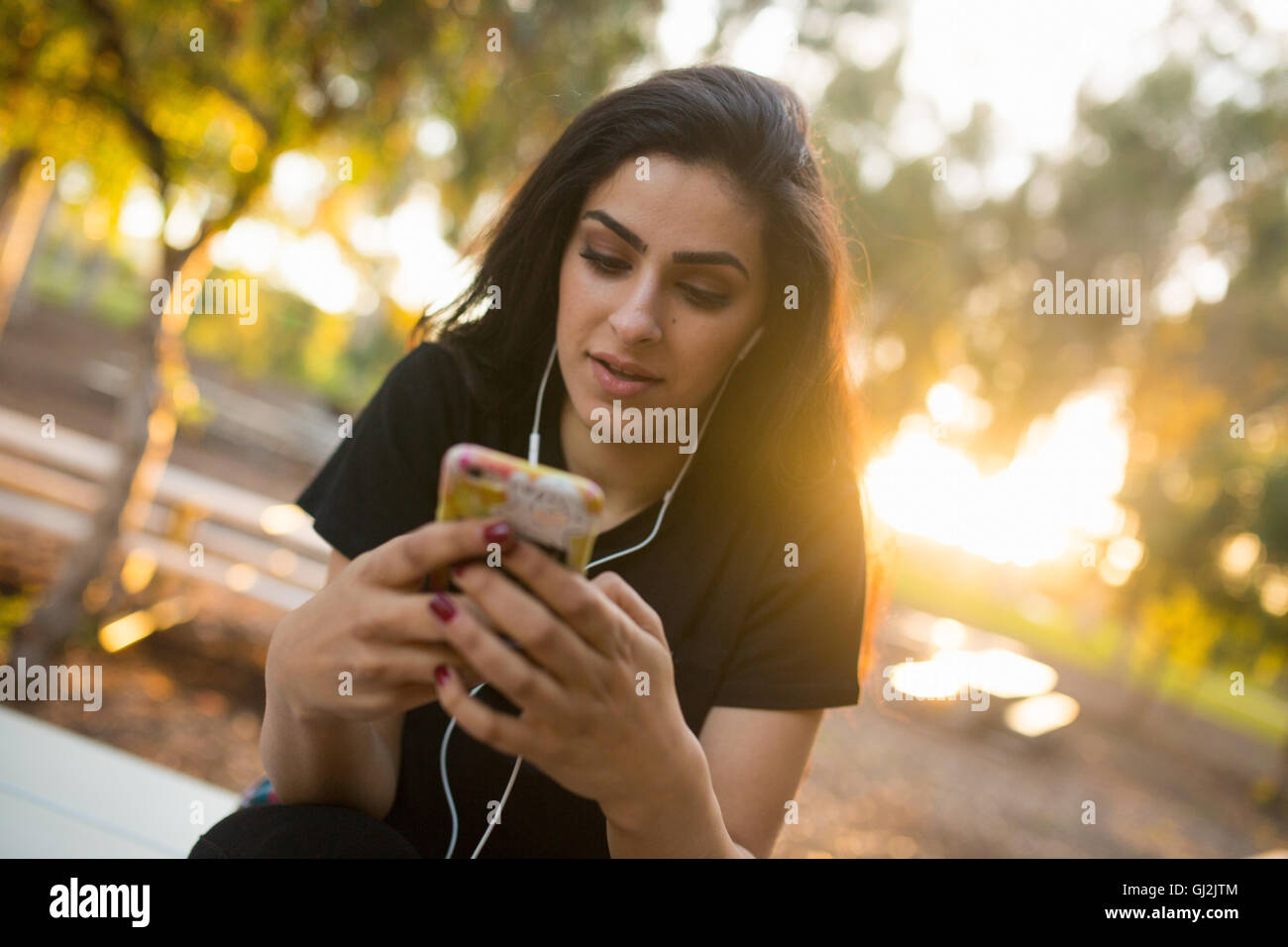 Jeune femme, à l'extérieur, le port d'écouteurs, holding smartphone Banque D'Images