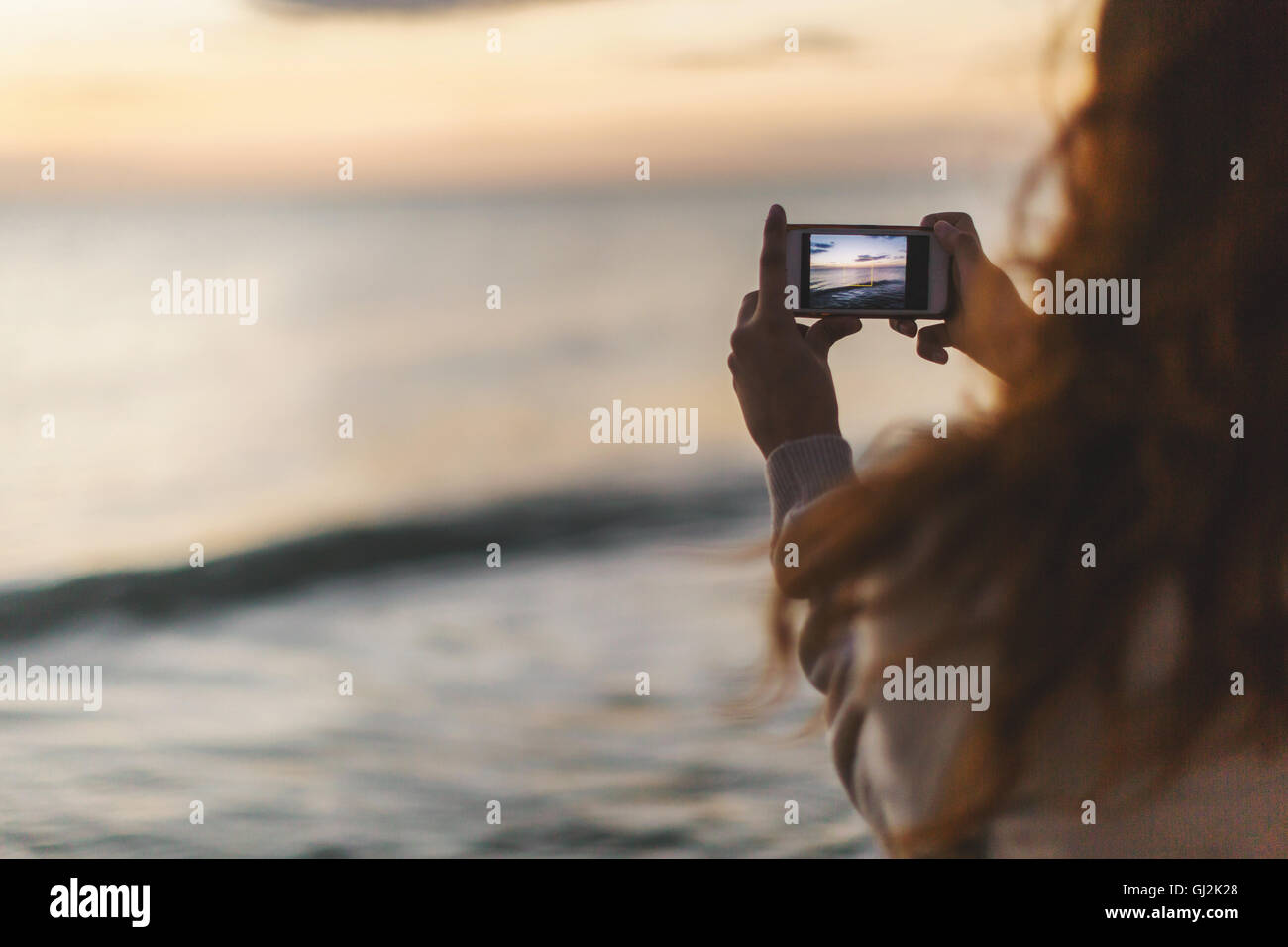 Woman taking photograph with mobile phone on beach Banque D'Images