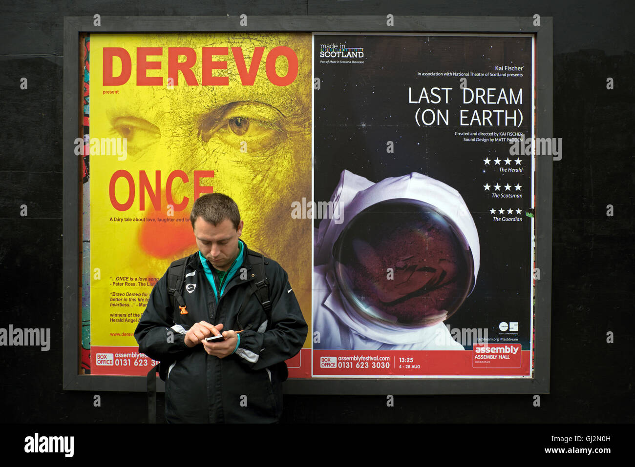Un homme à l'aide de son téléphone portable et se tenant devant Festival Fringe d'affiches. Banque D'Images
