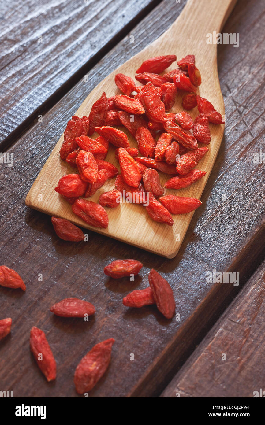 Baies de goji séchées en cuillère en bois sur fond de bois. Banque D'Images