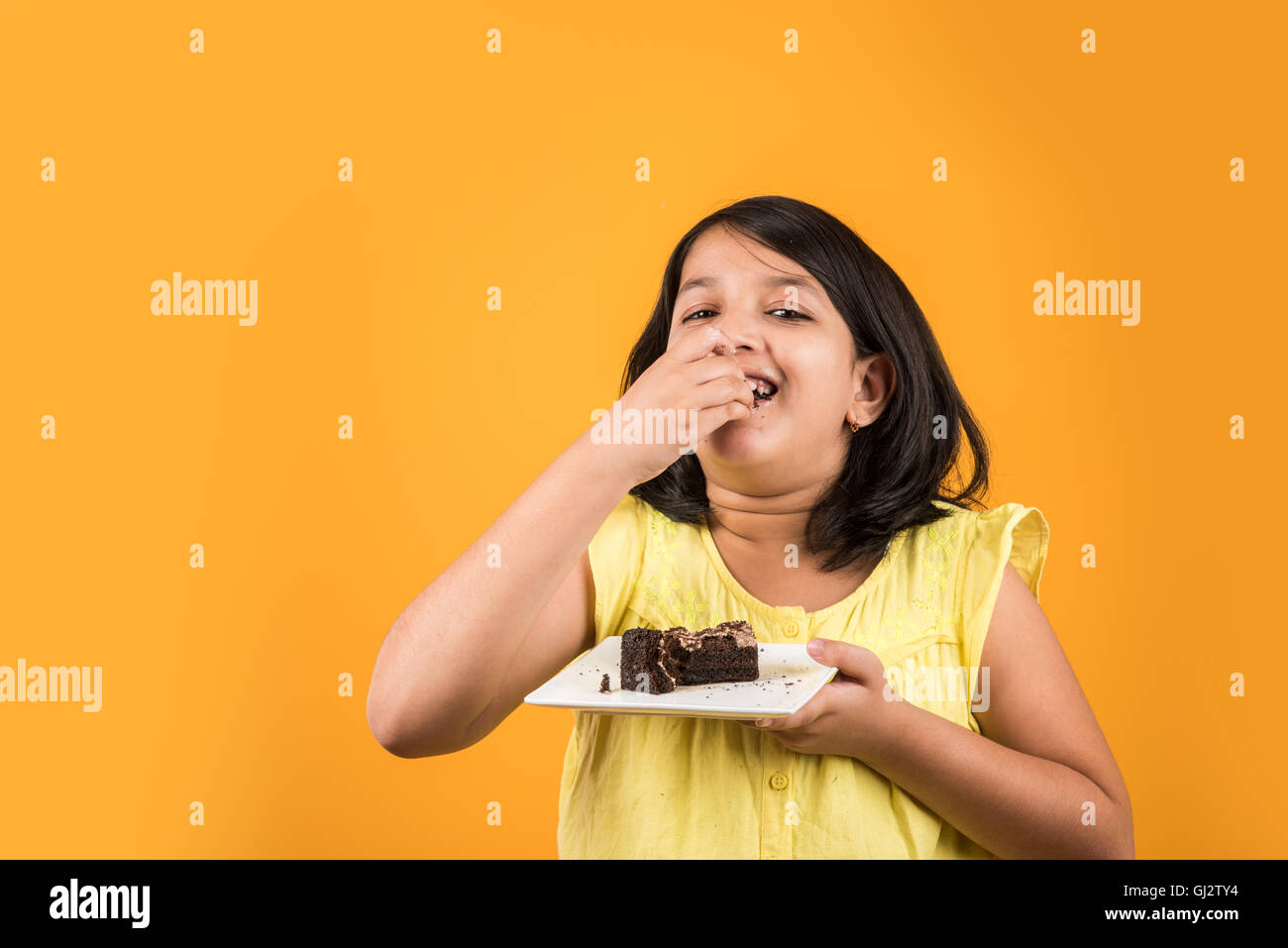 Portrait of Indian kid manger un gâteau ou une pâtisserie, cute little girl eating cake, girl eating chocolate cake sur fond coloré Banque D'Images