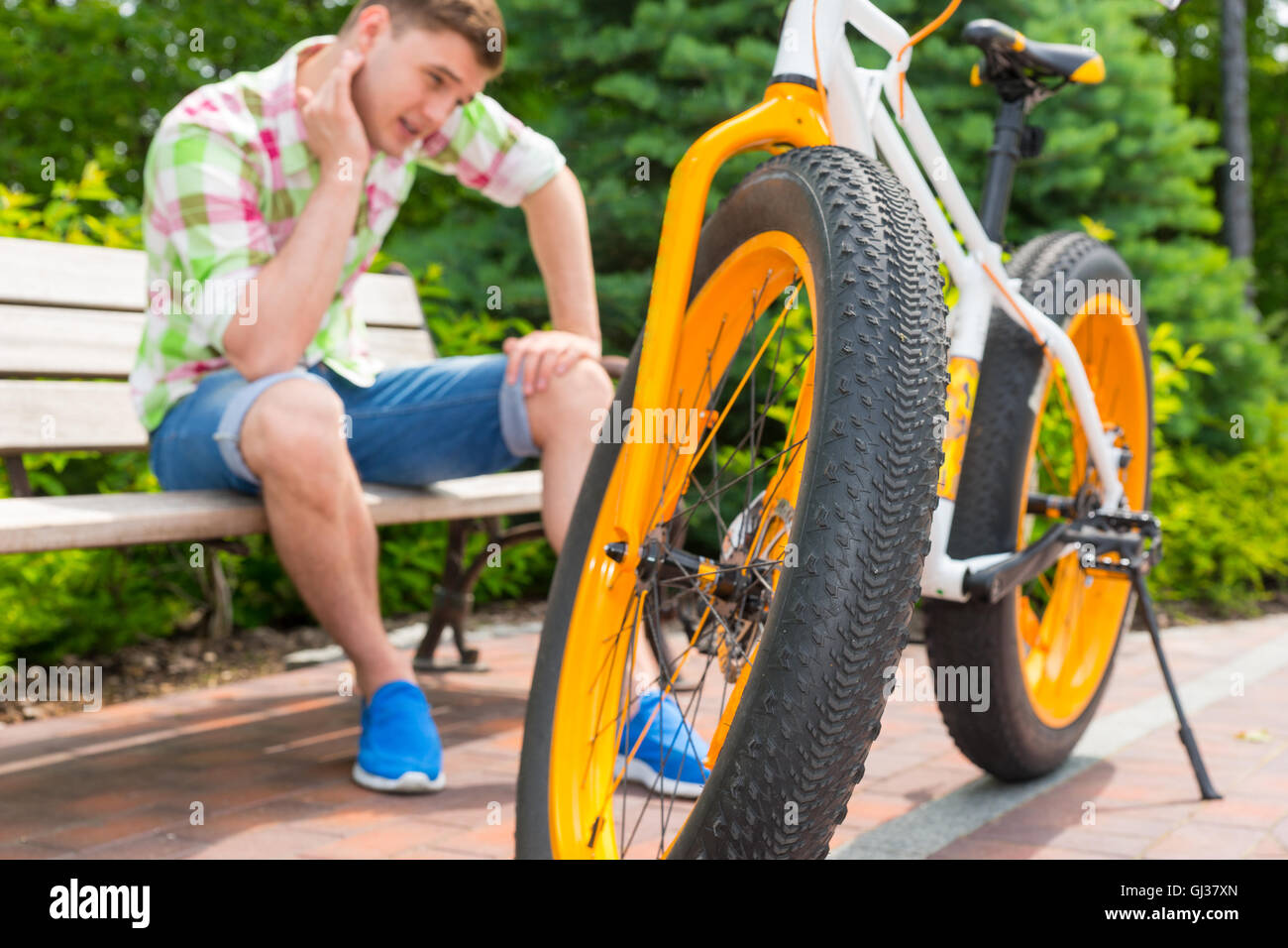 Homme assis avec expression triste assis sur un banc près de vélo, se  concentrer sur la roue dans un beau parc vert Photo Stock - Alamy