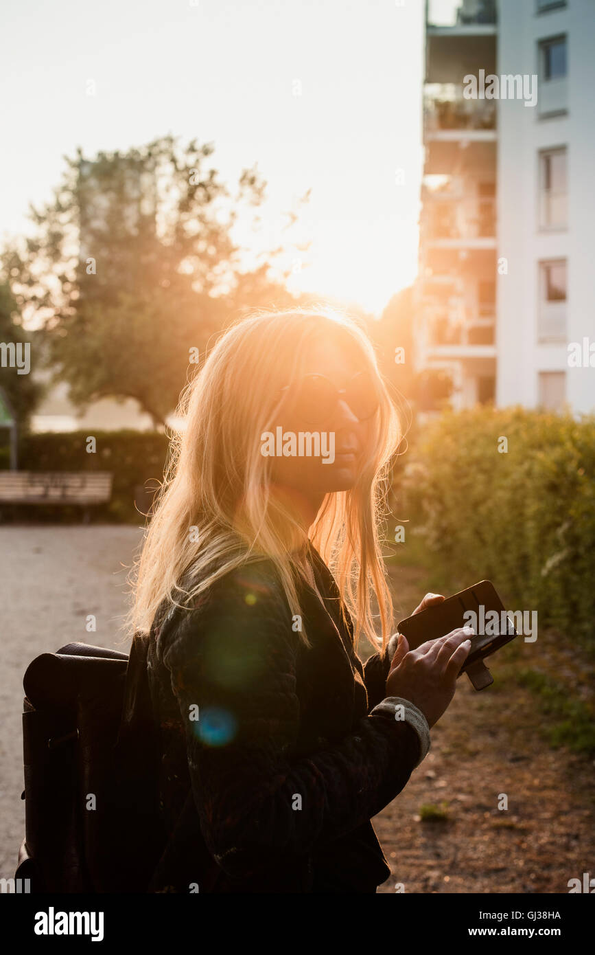 Jeune femme à l'extérieur, au coucher du soleil, using smartphone Banque D'Images