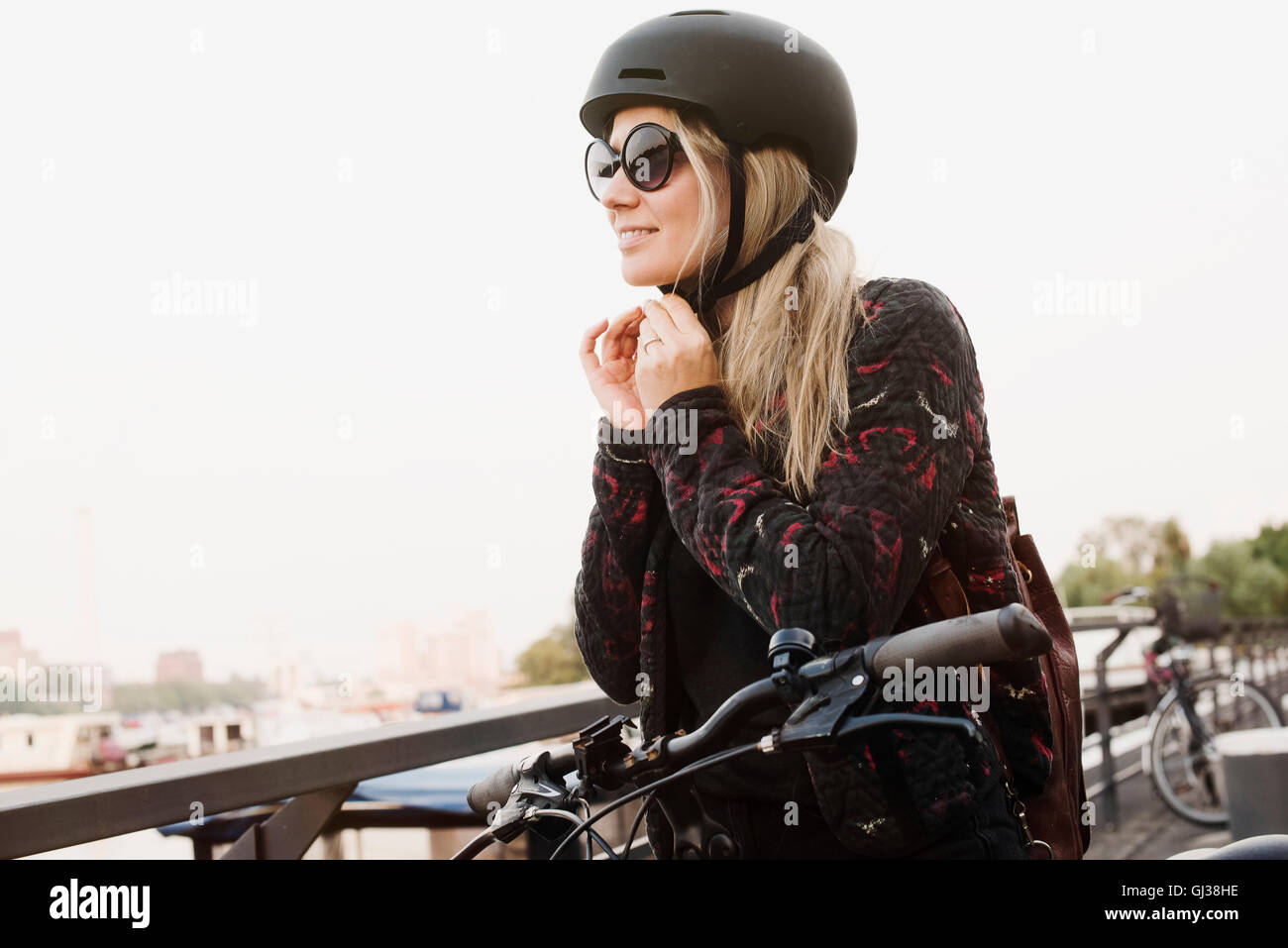 Jeune femme à l'extérieur, mettre sur casque, prêt à circuler à bicyclette Banque D'Images