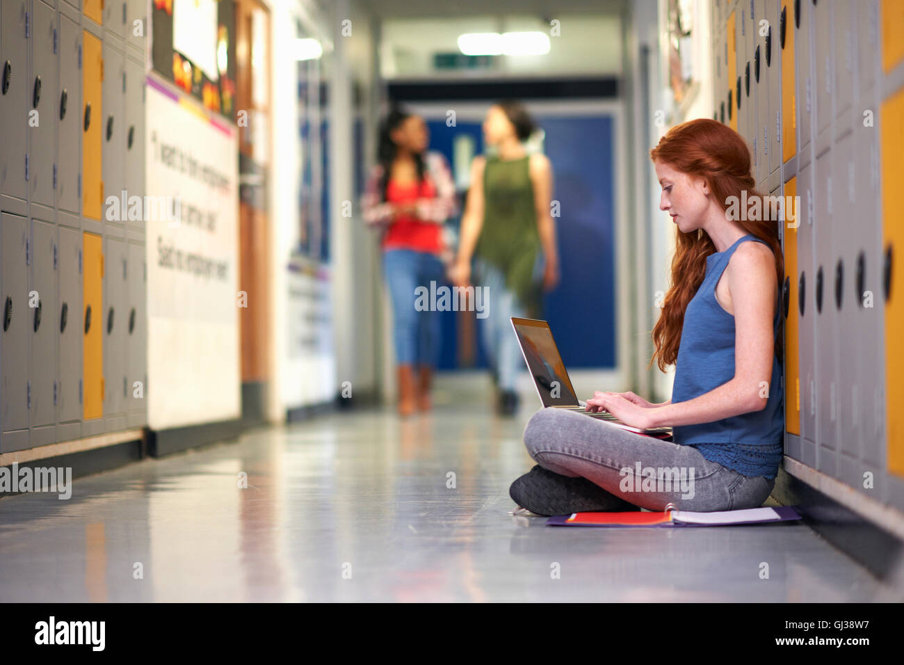 Young female college student sitting on vestiaire étage typing on laptop Banque D'Images