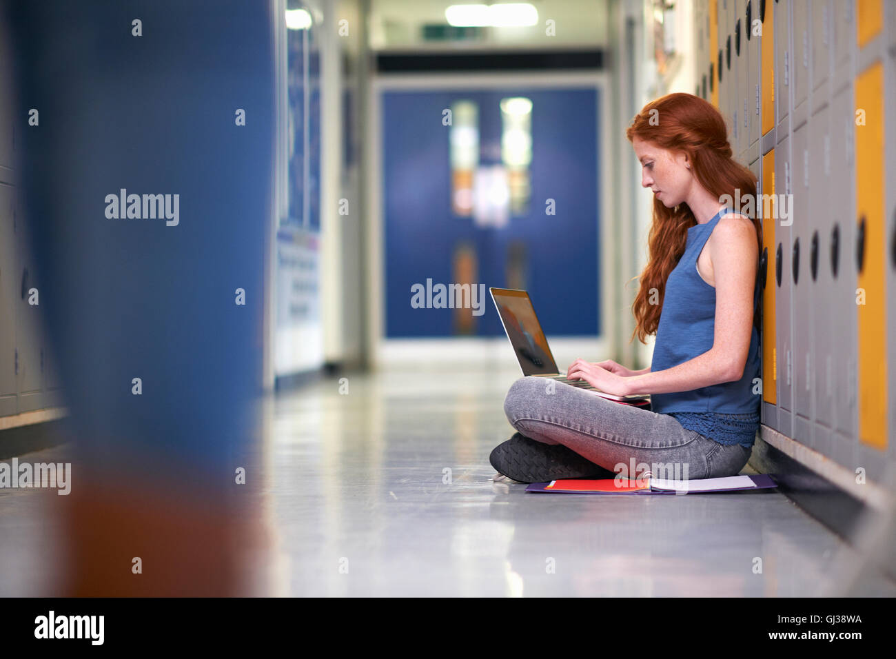 Young female college student sitting on vestiaire étage typing on laptop Banque D'Images