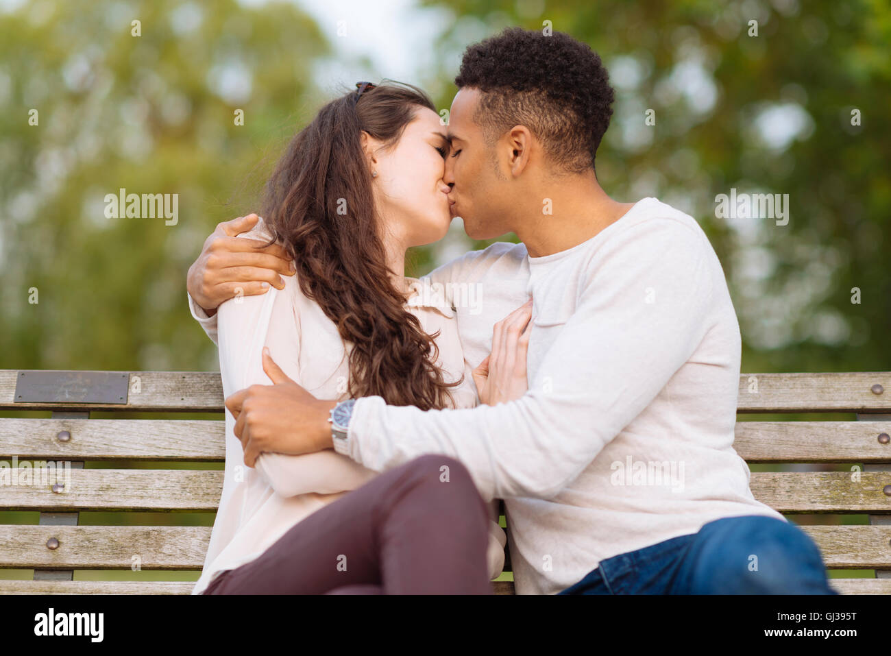 Jeune couple sur banc de parc s'embrasser Banque D'Images
