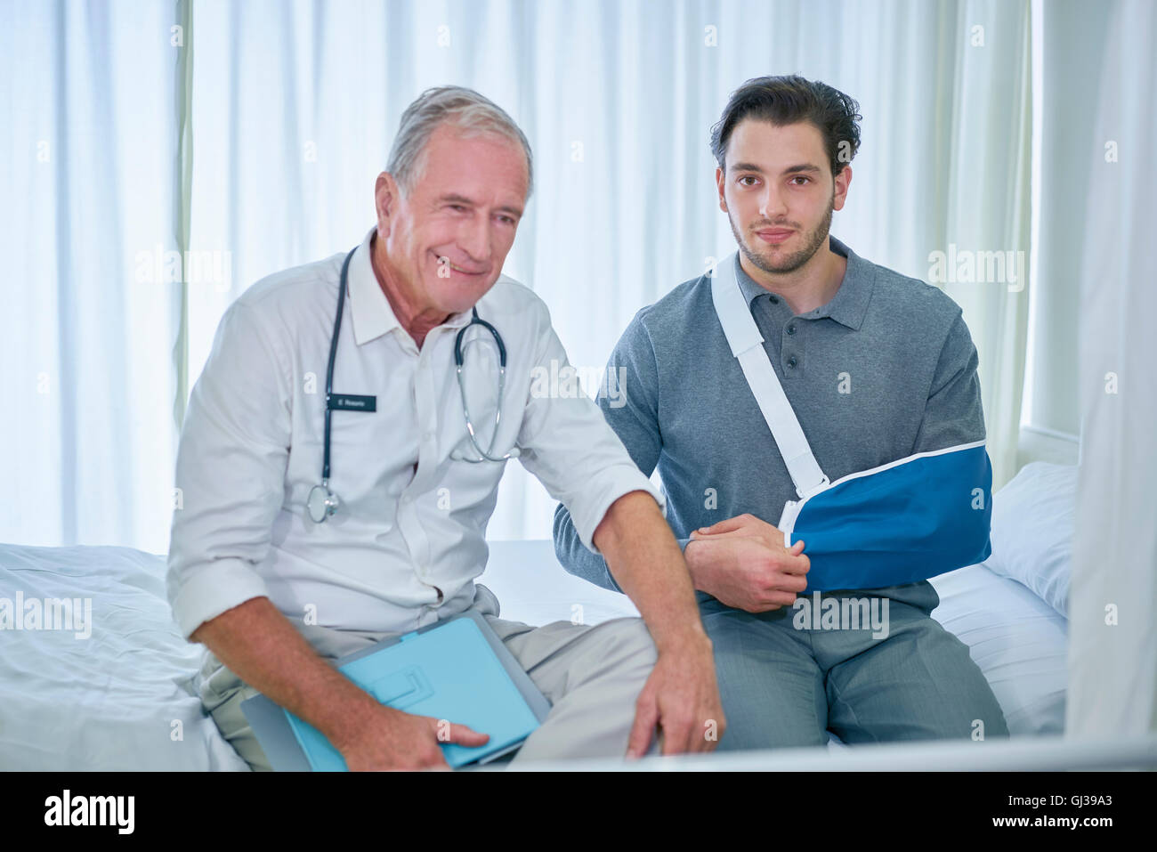Médecin et l'homme avec le bras en écharpe assis sur lit d'hôpital Banque D'Images