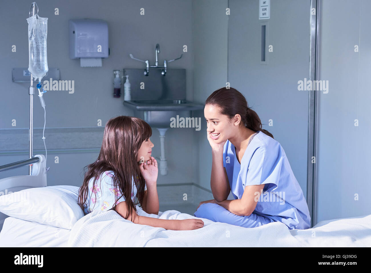 Nurse talking with girl patient assis dans son lit à l'hôpital de pédiatrie Banque D'Images