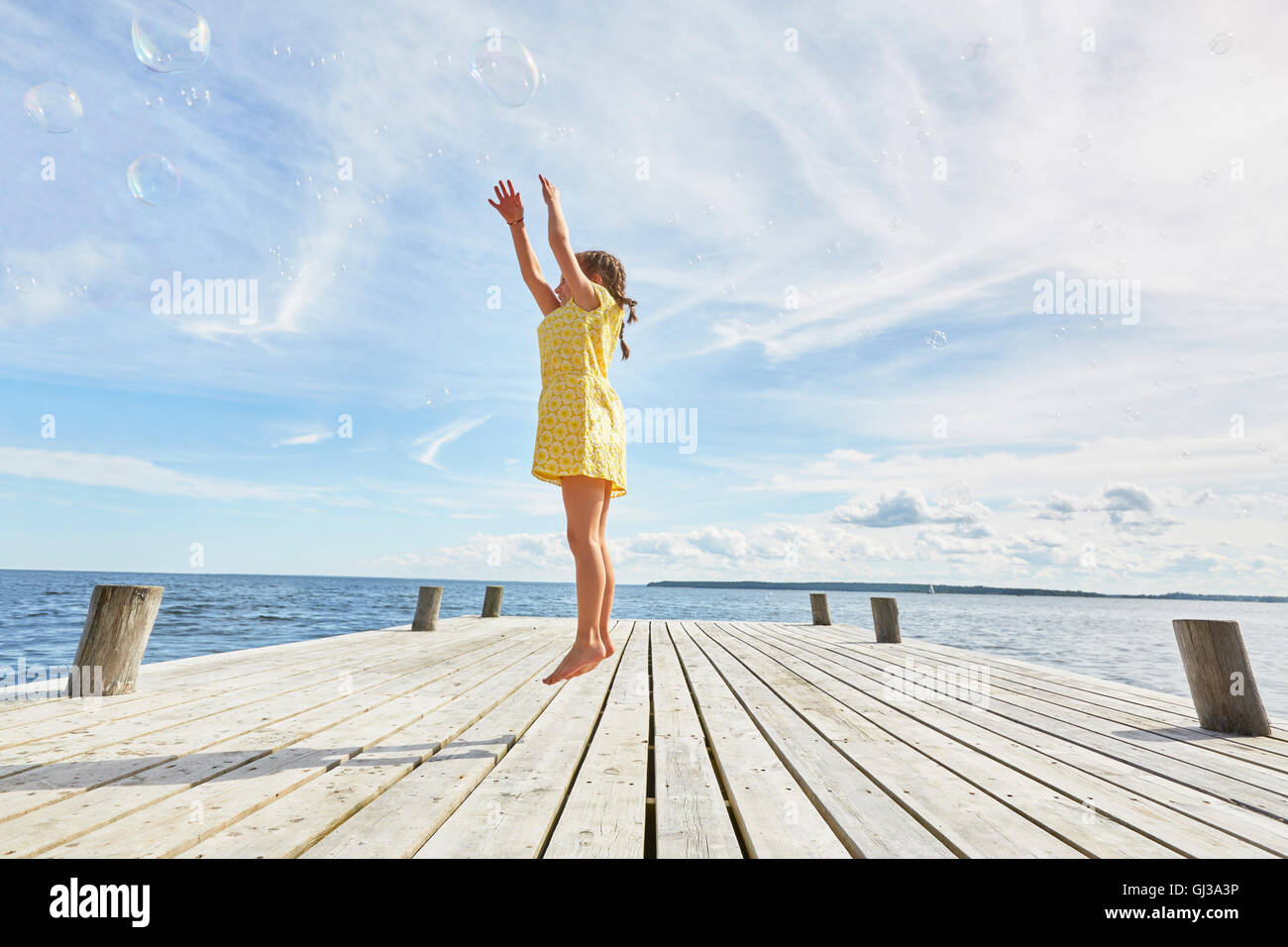 Jeune fille sur la jetée en bois, sauter pour atteindre bubbles Banque D'Images