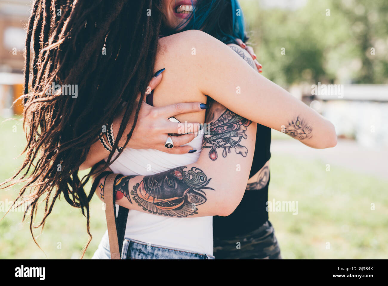 Les jeunes femmes tatouées hugging in urban park Banque D'Images