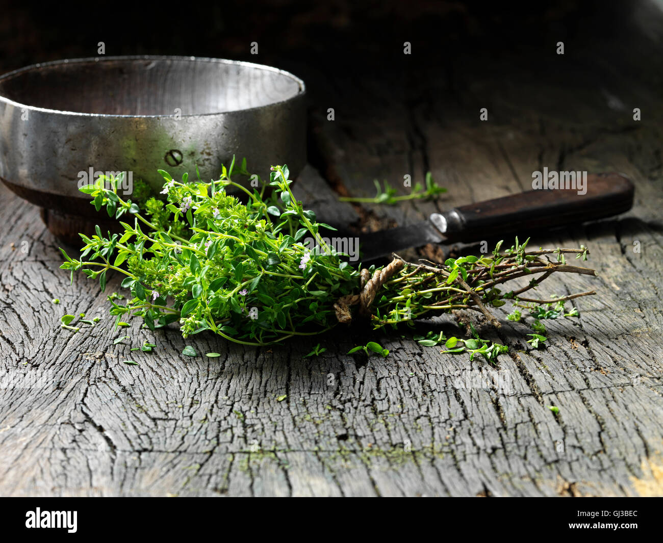 Les feuilles de thym attachés ensemble avec de la ficelle, vintage bol en métal et le couteau sur la surface en bois rustique Banque D'Images