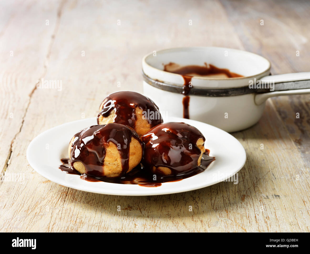 Profiteroles sauce chocolat chaud sur assiette blanche, table en bois rustique Banque D'Images